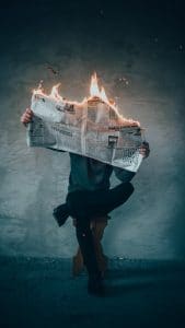 A man sitting on a chair with a newspaper on fire