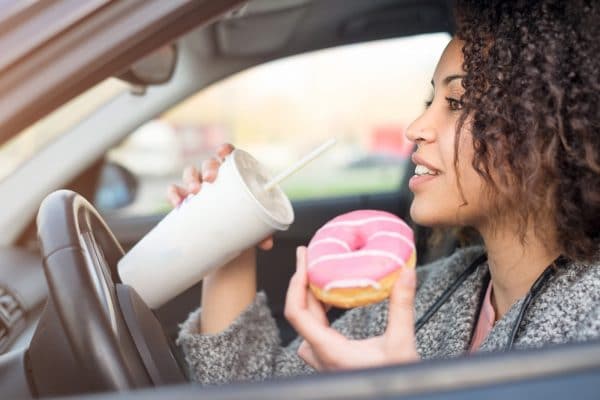 Woman eating a sweet and drinking driving her car
