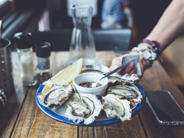 A person is holding a plate of oysters on a table