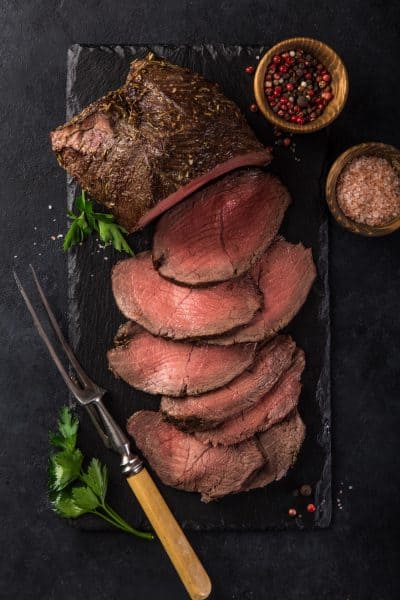 Sliced beef on a black slate board with herbs and spices