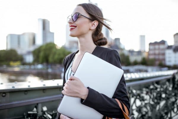 Portrait of a young businesswoman with laptop standing on the bridge in Frankfurt city