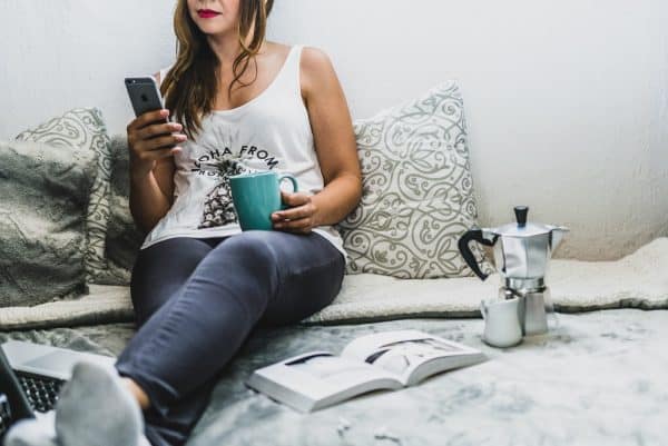 A woman sitting on a bed with a cup of coffee and a cell phone