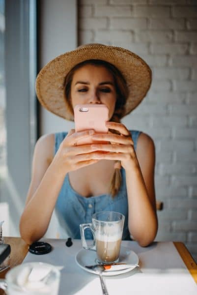 A woman in a hat is using her phone while sitting at a table