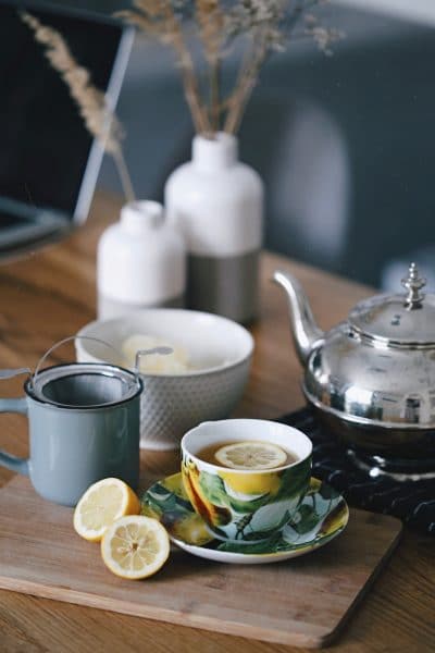 A tea pot, a cup, a lemon and a laptop on a wooden table