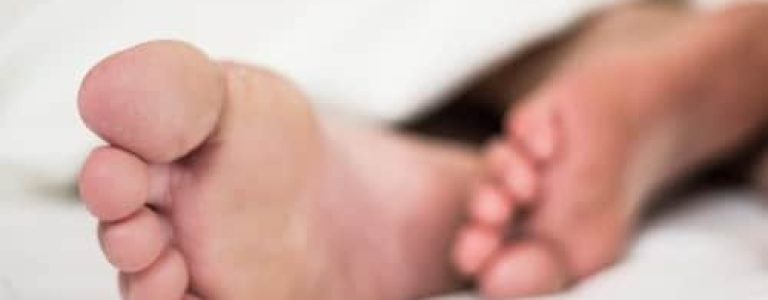 A person's feet are laying on a bed